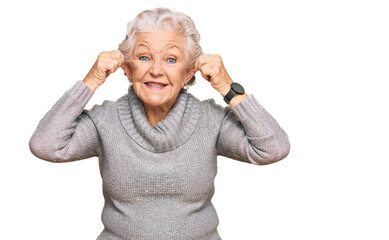 Senior grey-haired woman wearing casual winter sweater smiling pulling ears with fingers, funny...