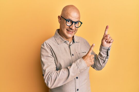 Middle age bald man wearing casual clothes and glasses smiling and looking at the camera pointing with two hands and fingers to the side.