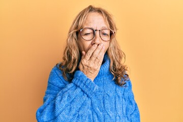 Middle age blonde woman wearing glasses and casual winter sweater bored yawning tired covering mouth with hand. restless and sleepiness.