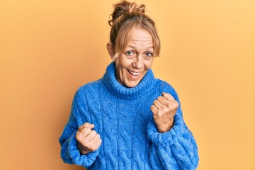 Middle age blonde woman wearing casual winter sweater celebrating surprised and amazed for success with arms raised and eyes closed