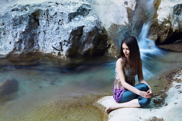 Young slim caucasian woman with long brown hair doing yoga in the mountains near a mountain river.