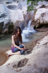 Young slim caucasian woman with long brown hair doing yoga in the mountains near a mountain river.