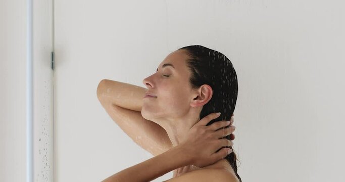 Head shot beautiful millennial woman taking morning shower, washing wet hair massaging sculp under warm water, rinsing off moisturizing conditioner treatment mask, enjoying daily hygienic routine.