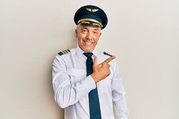 Handsome middle age mature man wearing airplane pilot uniform cheerful with a smile on face pointing with hand and finger up to the side with happy and natural expression