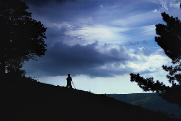 Silhouette of a professional landscape photographer in the mountains at sunset.
