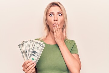 Young beautiful blonde woman holding bunch of dollars banknotes over white background covering...