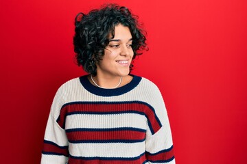 Fototapeta na wymiar Young hispanic woman with curly hair wearing casual winter sweater looking to side, relax profile pose with natural face and confident smile.