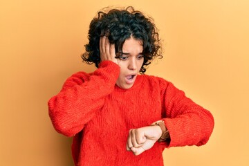 Young hispanic woman with curly hair wearing casual winter sweater looking at the watch time...
