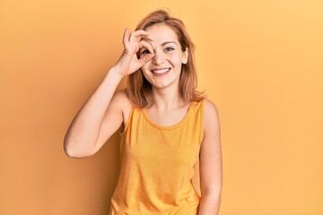 Young caucasian woman wearing casual style with sleeveless shirt doing ok gesture with hand smiling, eye looking through fingers with happy face.