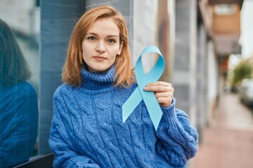 Young caucasian girl with serious expression holding blue awareness ribbon at the city.