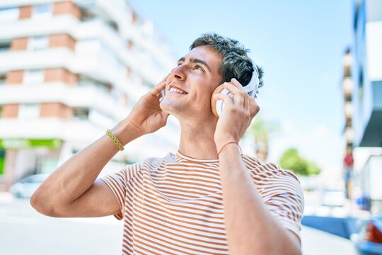 Young handsome caucasian man smiling happy listening to music using headphones walking at city.