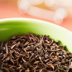 Closeup of dried black tea leaves in a green cup on a table