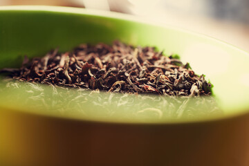 Closeup of dried black tea leaves in a green cup on a table