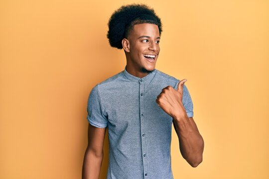 African american man with afro hair wearing casual clothes pointing thumb up to the side smiling happy with open mouth