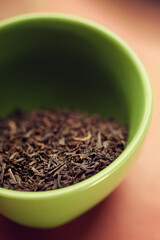 Closeup of dried black tea leaves in a green cup on a table