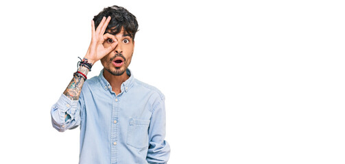 Young hispanic man wearing casual clothes doing ok gesture shocked with surprised face, eye looking through fingers. unbelieving expression.