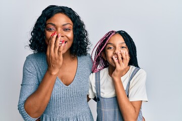 Beautiful african american mother and daughter wearing casual clothes and hugging laughing and embarrassed giggle covering mouth with hands, gossip and scandal concept