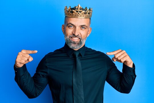 Middle age handsome business man wearing king crown looking confident with smile on face, pointing oneself with fingers proud and happy.