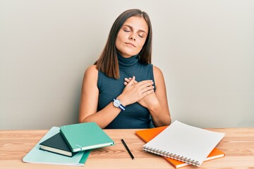 Naklejka premium Young caucasian woman studying for exam smiling with hands on chest, eyes closed with grateful gesture on face. health concept.