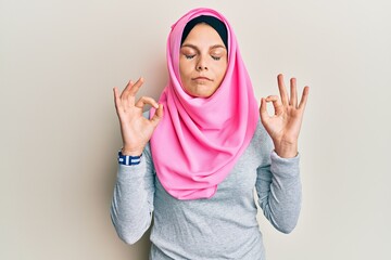 Young caucasian woman wearing traditional islamic hijab scarf relax and smiling with eyes closed doing meditation gesture with fingers. yoga concept.