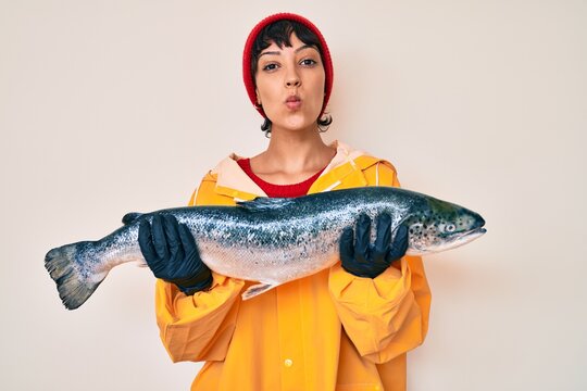 Beautiful brunettte fisher woman wearing raincoat holding fresh salmon looking at the camera blowing a kiss being lovely and sexy. love expression.