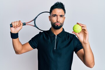 Young man with beard playing tennis holding racket and ball looking at the camera blowing a kiss being lovely and sexy. love expression.