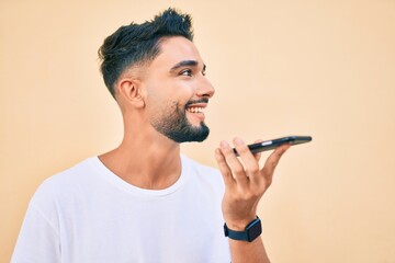 Young arab man smiling happy sending voice message using smartphone at the city.