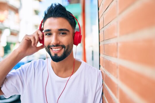 Young arab man smiling happy using headphones leaning on the wall at the city.