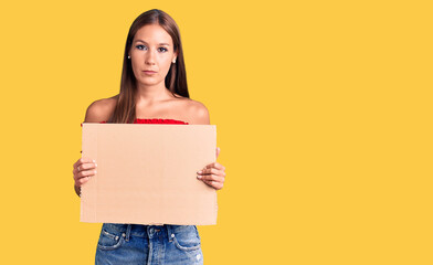 Young beautiful hispanic woman holding banner cardboard thinking attitude and sober expression looking self confident