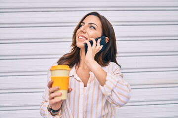 Young hispanic woman smiling happy talking on the smartphone and drinking take away coffee at the city.