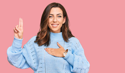 Young brunette woman wearing casual winter sweater smiling swearing with hand on chest and fingers...