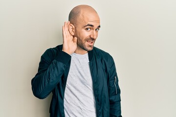 Young hispanic man wearing casual sporty jacket smiling with hand over ear listening and hearing to rumor or gossip. deafness concept.