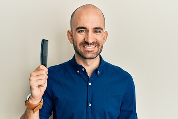 Young hispanic man holding comb loosing hair looking positive and happy standing and smiling with a...