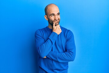 Young hispanic man wearing casual winter sweater thinking concentrated about doubt with finger on chin and looking up wondering