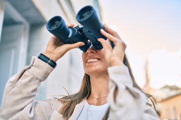 Young caucasian woman smiling happy looking for new opportunity using binoculars walking at the city.