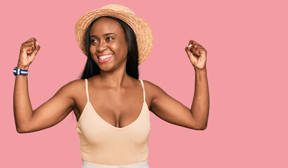 Young black woman wearing summer hat showing arms muscles smiling proud. fitness concept.