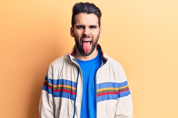 Young handsome man with beard wearing casual jacket sticking tongue out happy with funny expression. emotion concept.