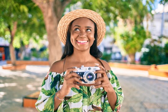 Young african american tourist woman on vacation smiling happy using vintage camera at the city.