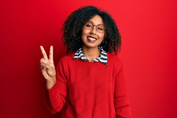 Beautiful african american woman with afro hair wearing sweater and glasses smiling looking to the...