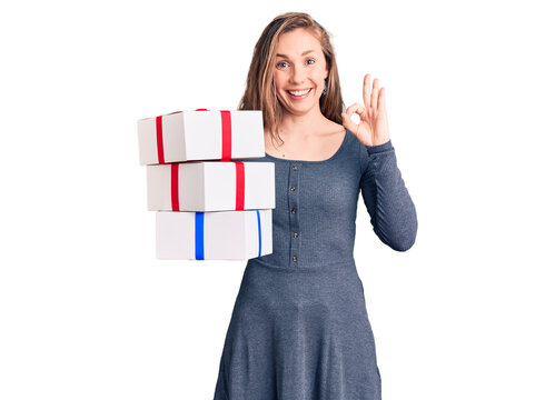 Young beautiful blonde woman holding birthday gift doing ok sign with fingers, smiling friendly gesturing excellent symbol