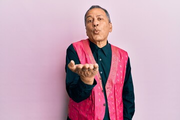 Middle age indian man wearing traditional indian clothes looking at the camera blowing a kiss with hand on air being lovely and sexy. love expression.