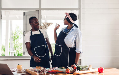Portrait of love african american couple having fun cooking together with fresh vegetable salad and...
