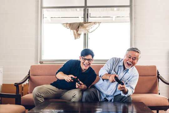 Portrait of happy love asian family senior mature father and young adult son having fun enjoying holding gamepad controller play console video game together at home