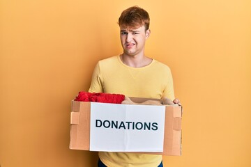 Young caucasian man holding donations box for charity clueless and confused expression. doubt...