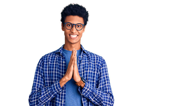 Young african american man wearing casual clothes and glasses praying with hands together asking for forgiveness smiling confident.