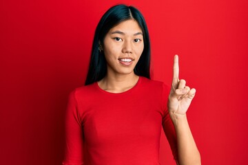 Young chinese woman wearing casual clothes smiling with an idea or question pointing finger up with happy face, number one