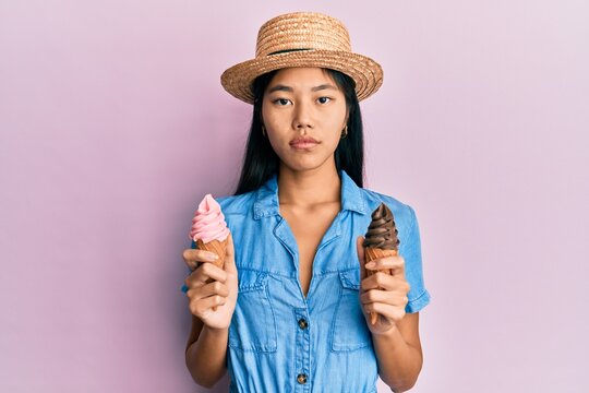 Young chinese woman wearing summer style holding ice cream relaxed with serious expression on face. simple and natural looking at the camera.
