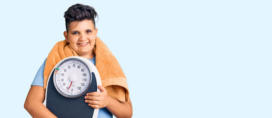 Little boy kid holding weight machine to balance weight loss looking positive and happy standing and smiling with a confident smile showing teeth