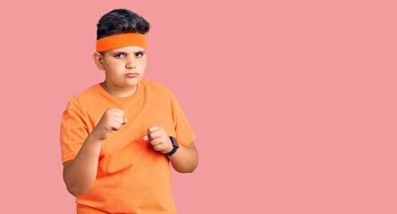 Little boy kid wearing sportswear ready to fight with fist defense gesture, angry and upset face,...