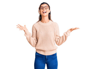 Young beautiful woman wearing casual winter sweater and glasses celebrating mad and crazy for success with arms raised and closed eyes screaming excited. winner concept